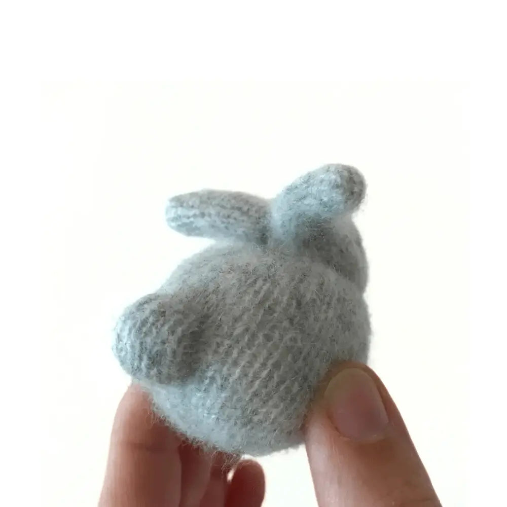 Small knitted bunny held in a hand against a white background