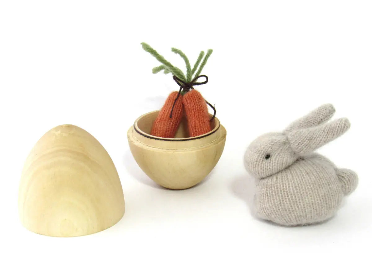 Knitted rabbit toy with a bowl of carrots and a shell on a white background