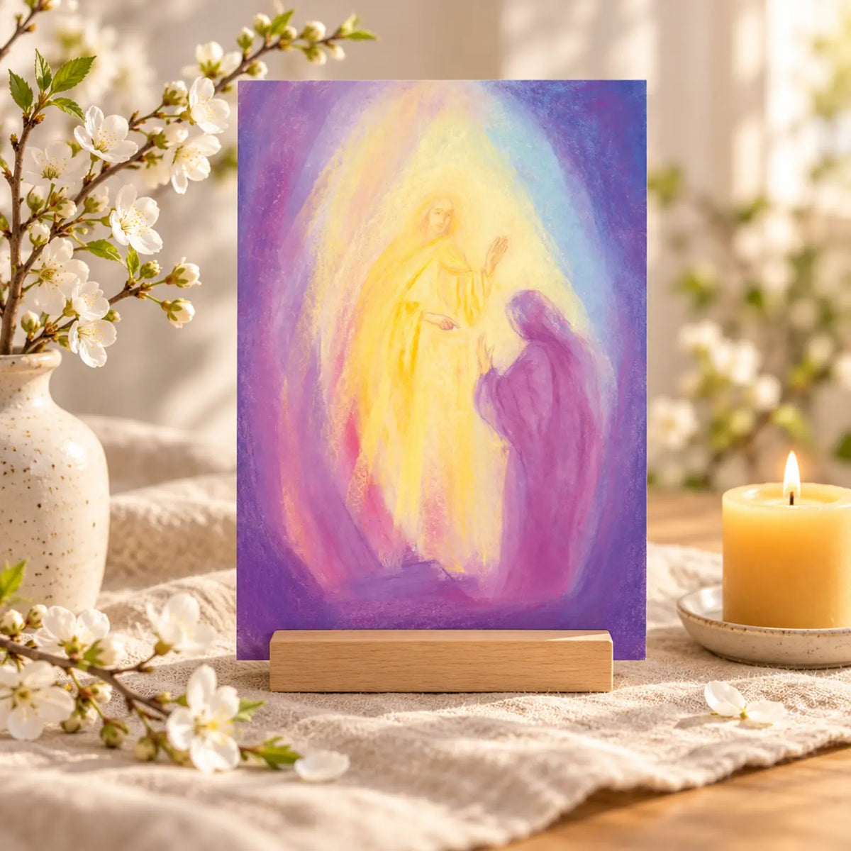 Easter Resurrection postcard by Marjan van Zeyl displayed in a wooden holder on natural linen, beside white spring blossoms and a glowing beeswax candle.