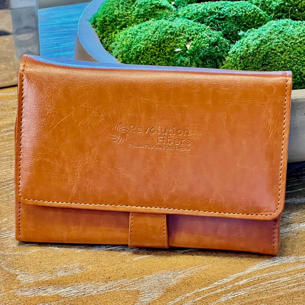 Brown leather wallet with 'Revolution Fibers' branding on a wooden surface with green plants in the background.
