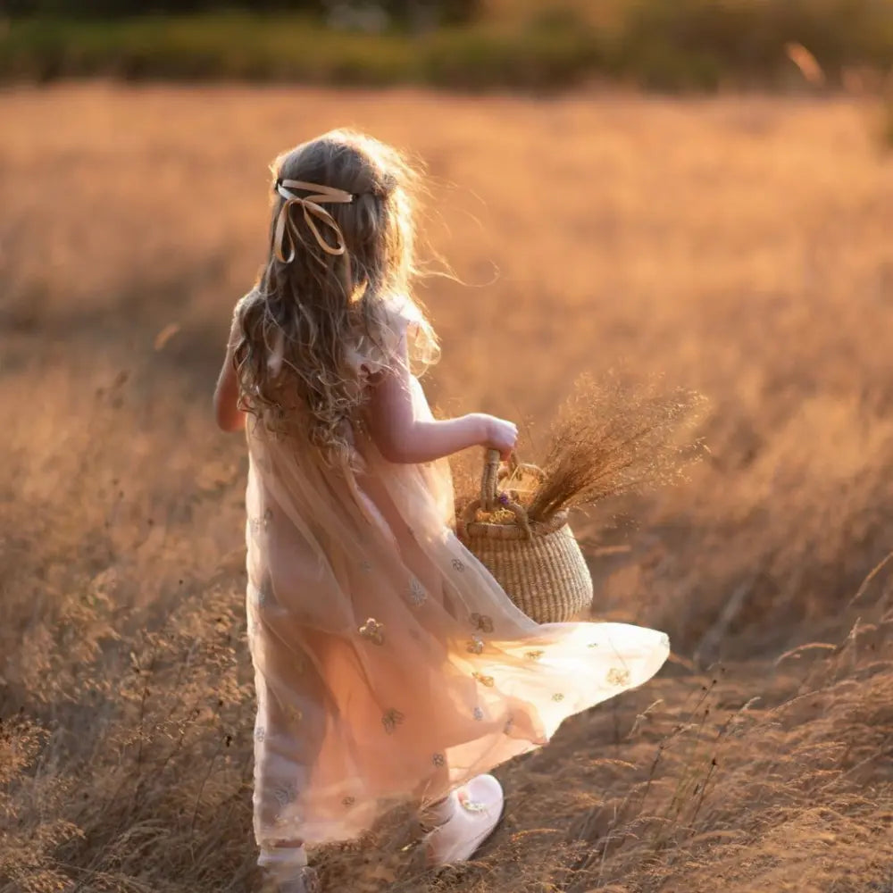 Young girl in a flowing dress holding a basket in a sunlit field