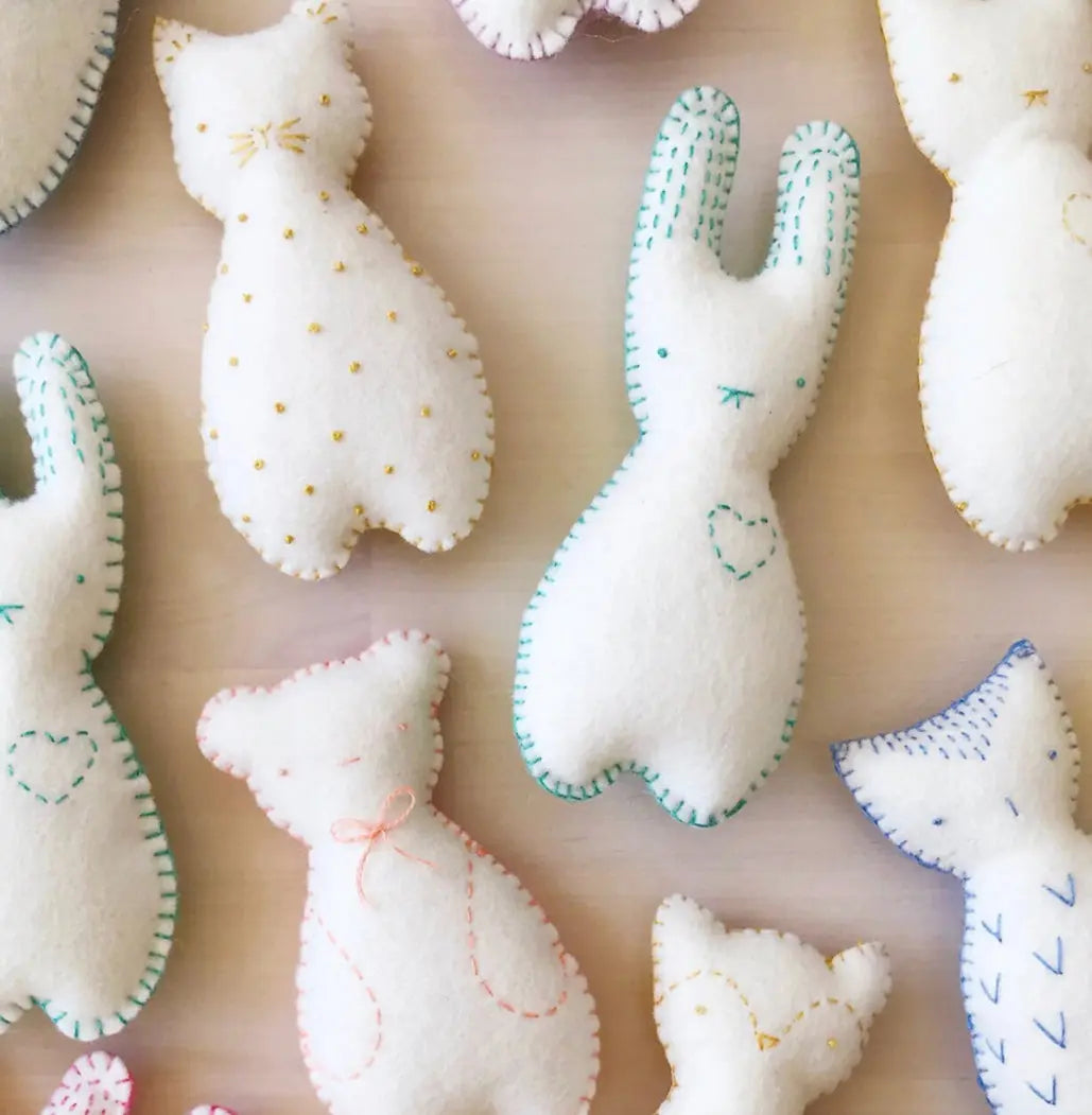 Collection of white pocket pals from embroidery kit with colorful stitching on a beige background