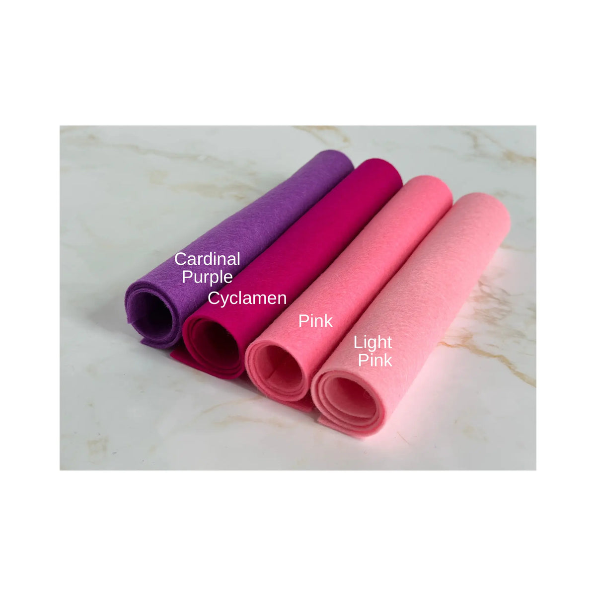100% Wool Felt rolls on a marble surface showing cardinal purple, cyclamen pink, pink, and light pink