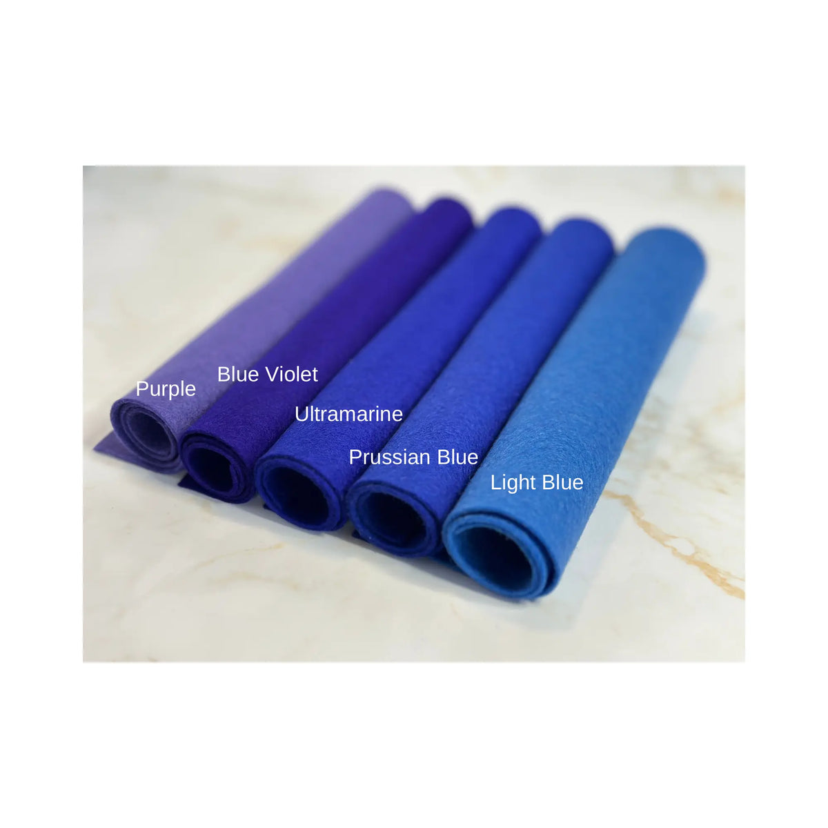100% Wool Felt rolls on a marble surface in colors purple, blue violet, ultramarine, Prussian blue, and light blue