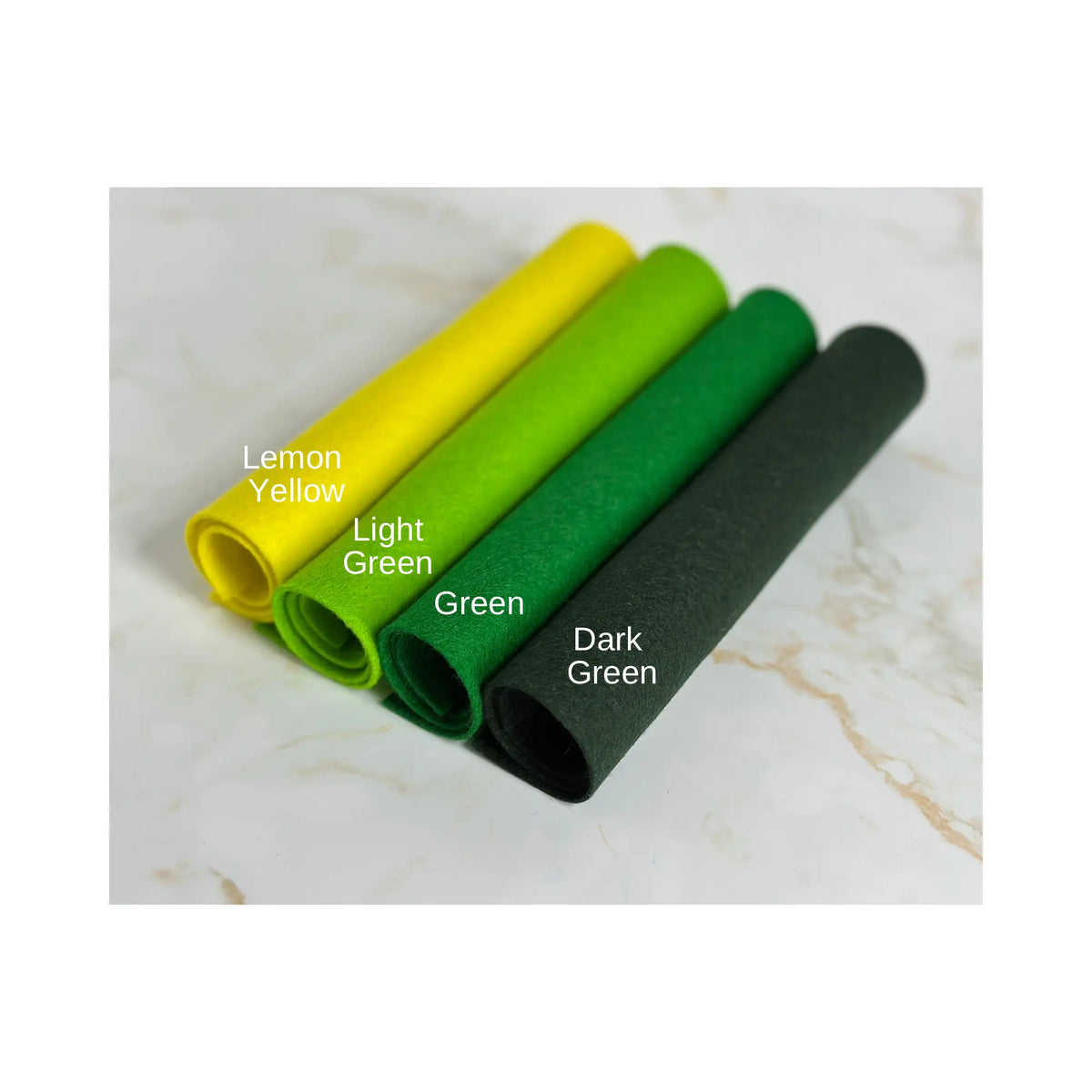 100% Wool Felt rolls on a marble surface showing lemon yellow, light green, green, and dark green