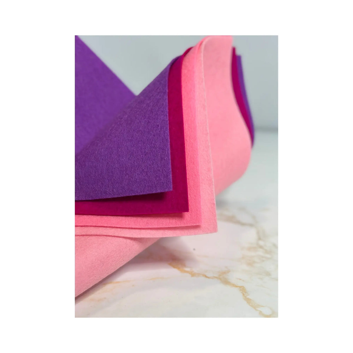 100% Wool Felt sheets layered to show the colors cardinal purple, cyclamen pink, pink, and light pink