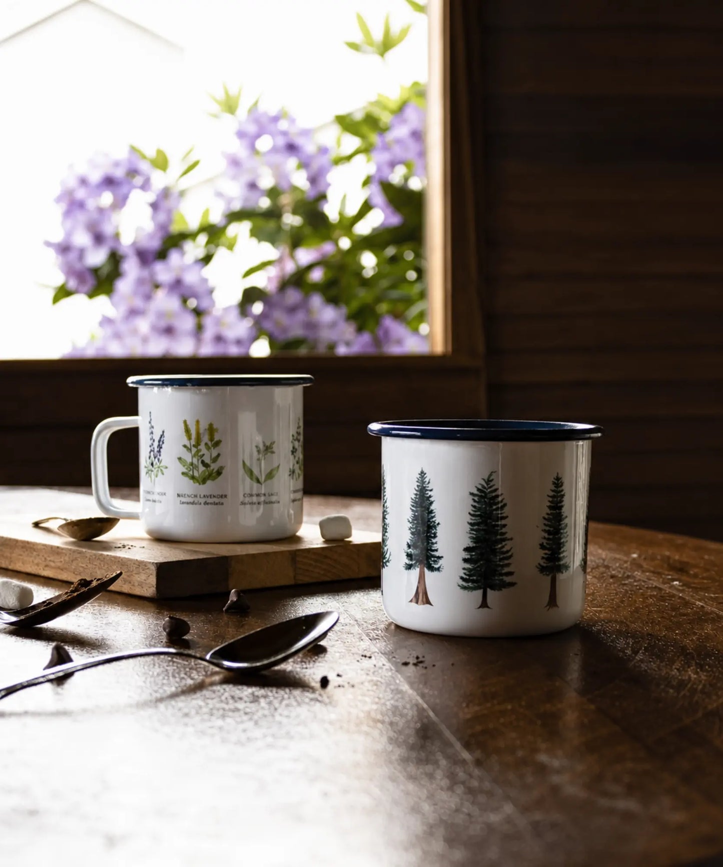 Two mugs on a wooden surface with a window in the background showing purple flowers.