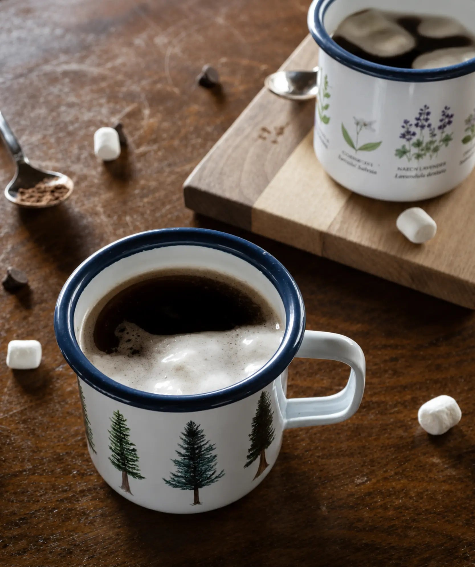Camp mugs with tree design filled with hot chocolate and marshmallows on a wooden surface