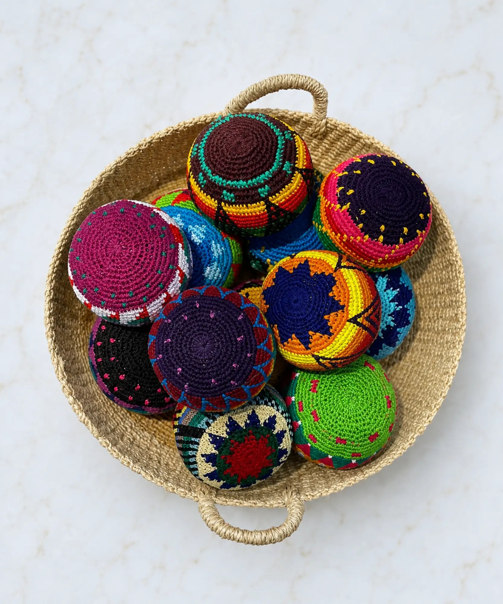 Colorful crocheted toss balls in a hacky sack shape and design stacked in a woven basket on a light background