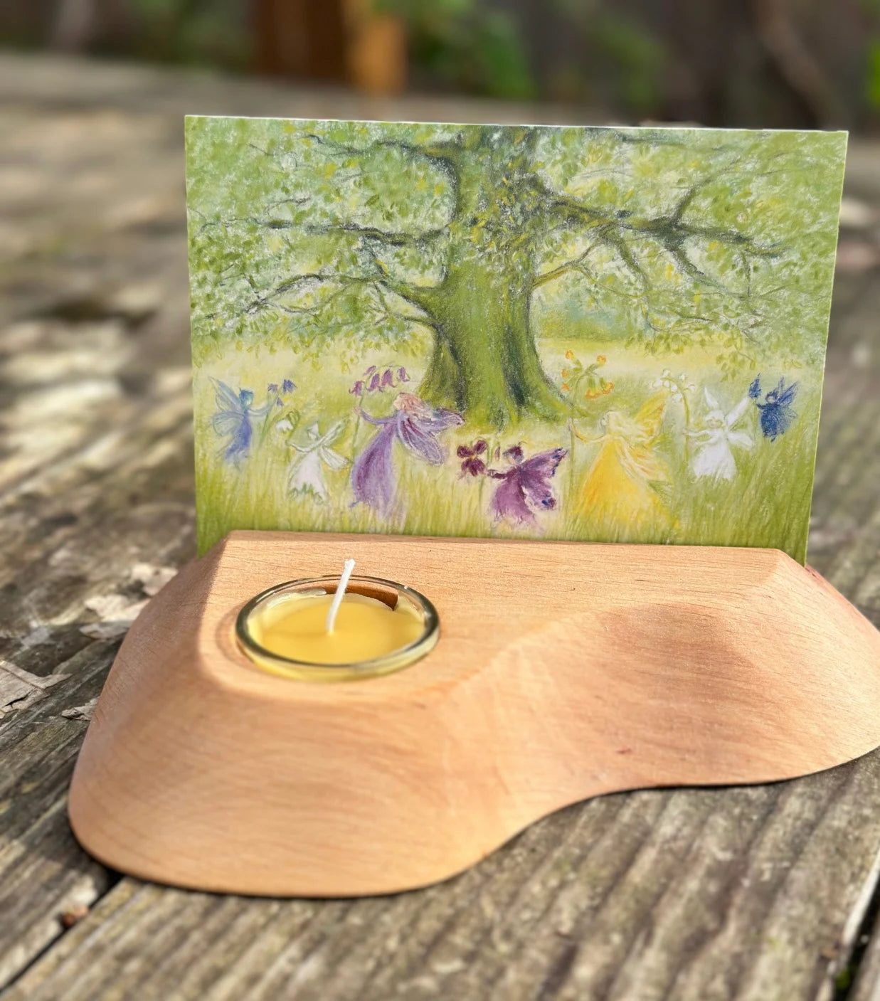 Fairies dancing around a tree postcard in a  wooden candle and postcard holder on a rustic tabletop