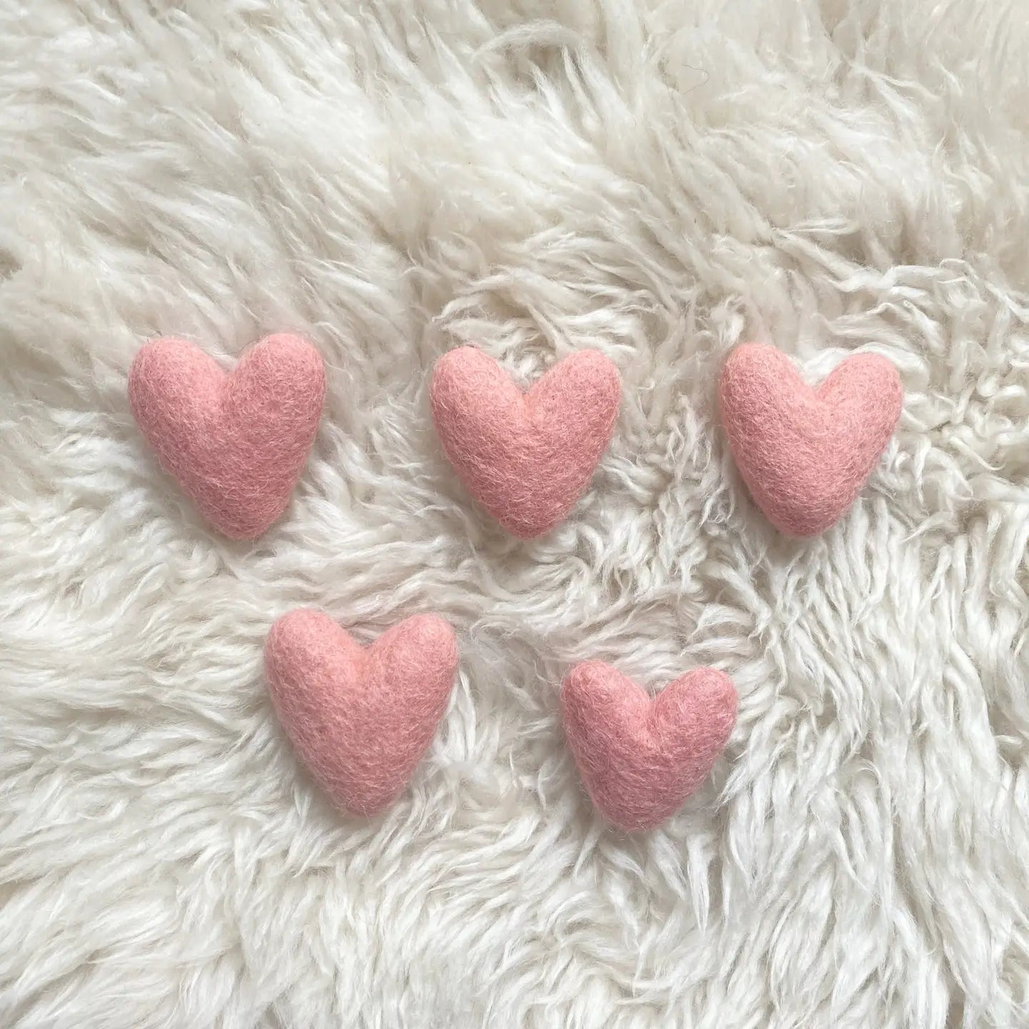 A collection of pink wool felt hearts placed on a fluffy white surface.