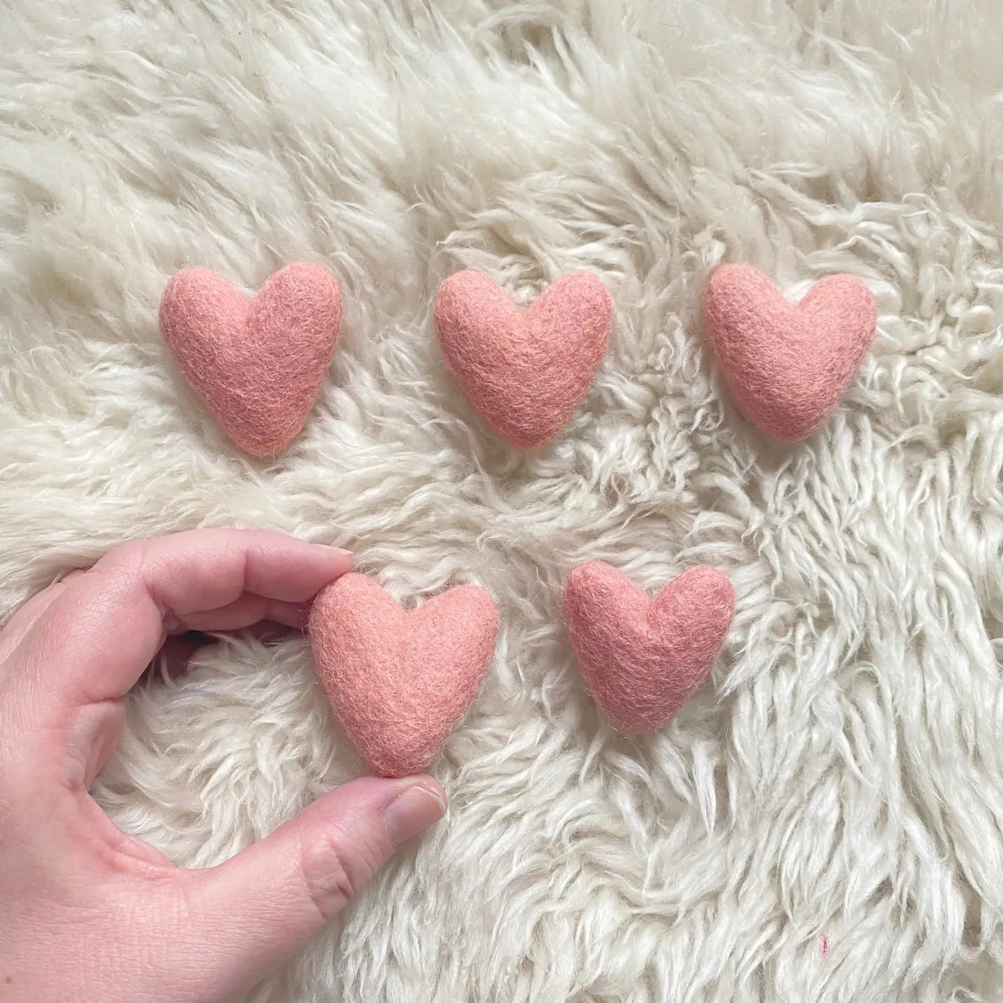 five wool felted pink hearts on a fleece with a hand holding one for size context