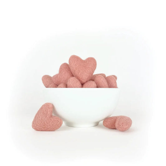 a white bowl of pink wool felted hearts on a white background