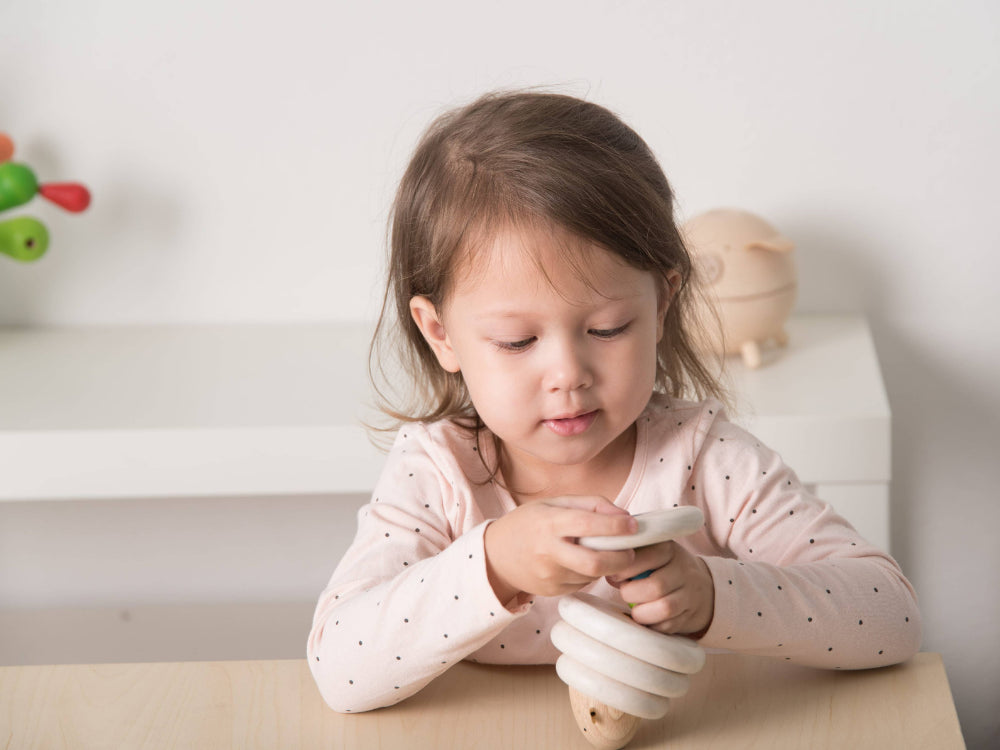 Child playing with a wooden lacing toy on a table against a white wall