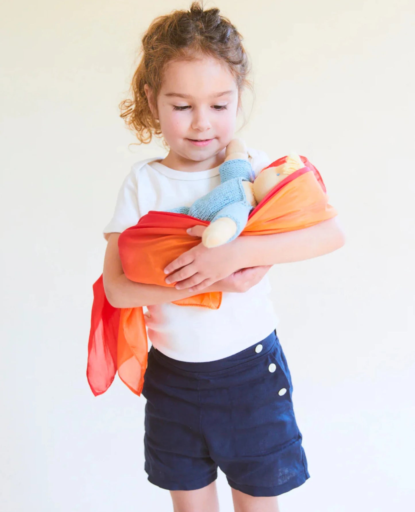 Girl using fire enchanted playsilk to wrap her baby doll in her arms