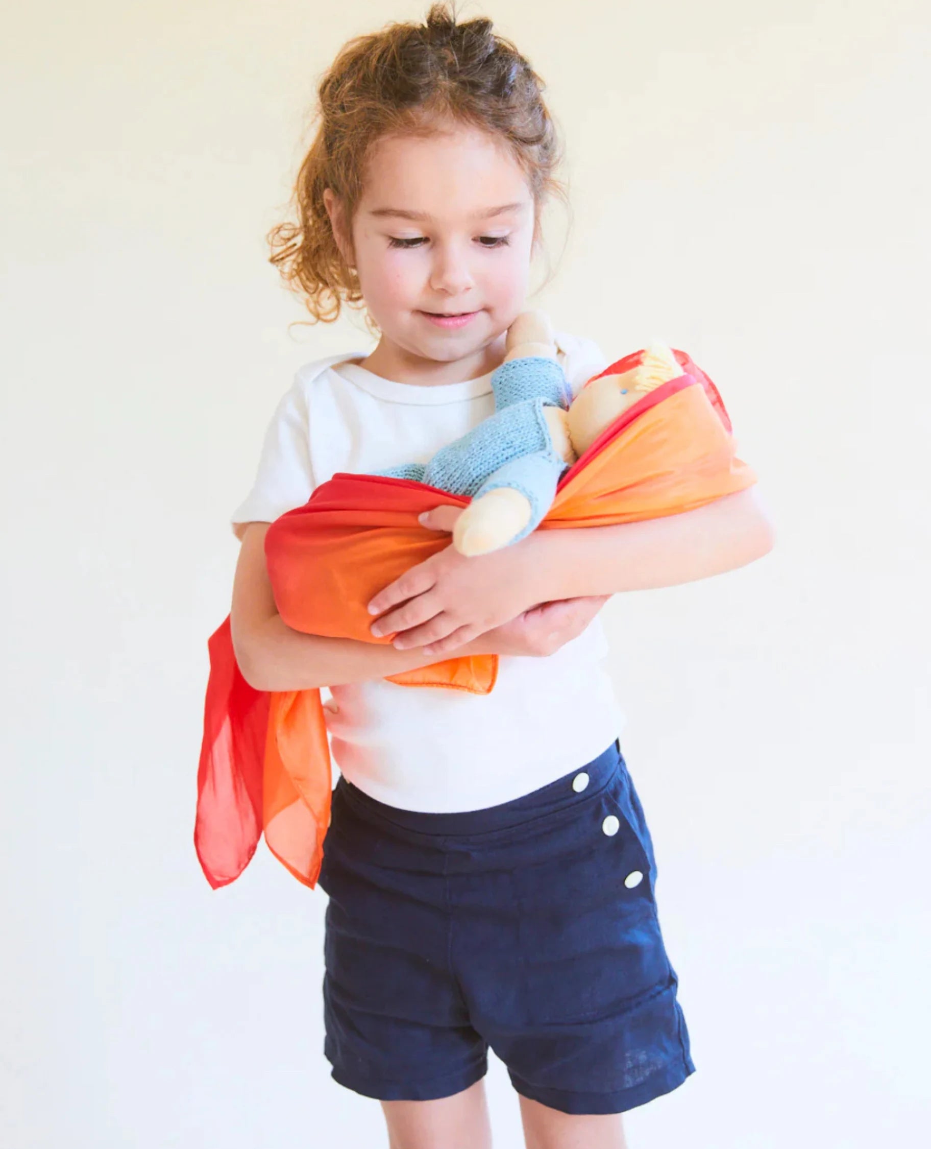 Girl using fire enchanted playsilk to wrap her baby doll in her arms