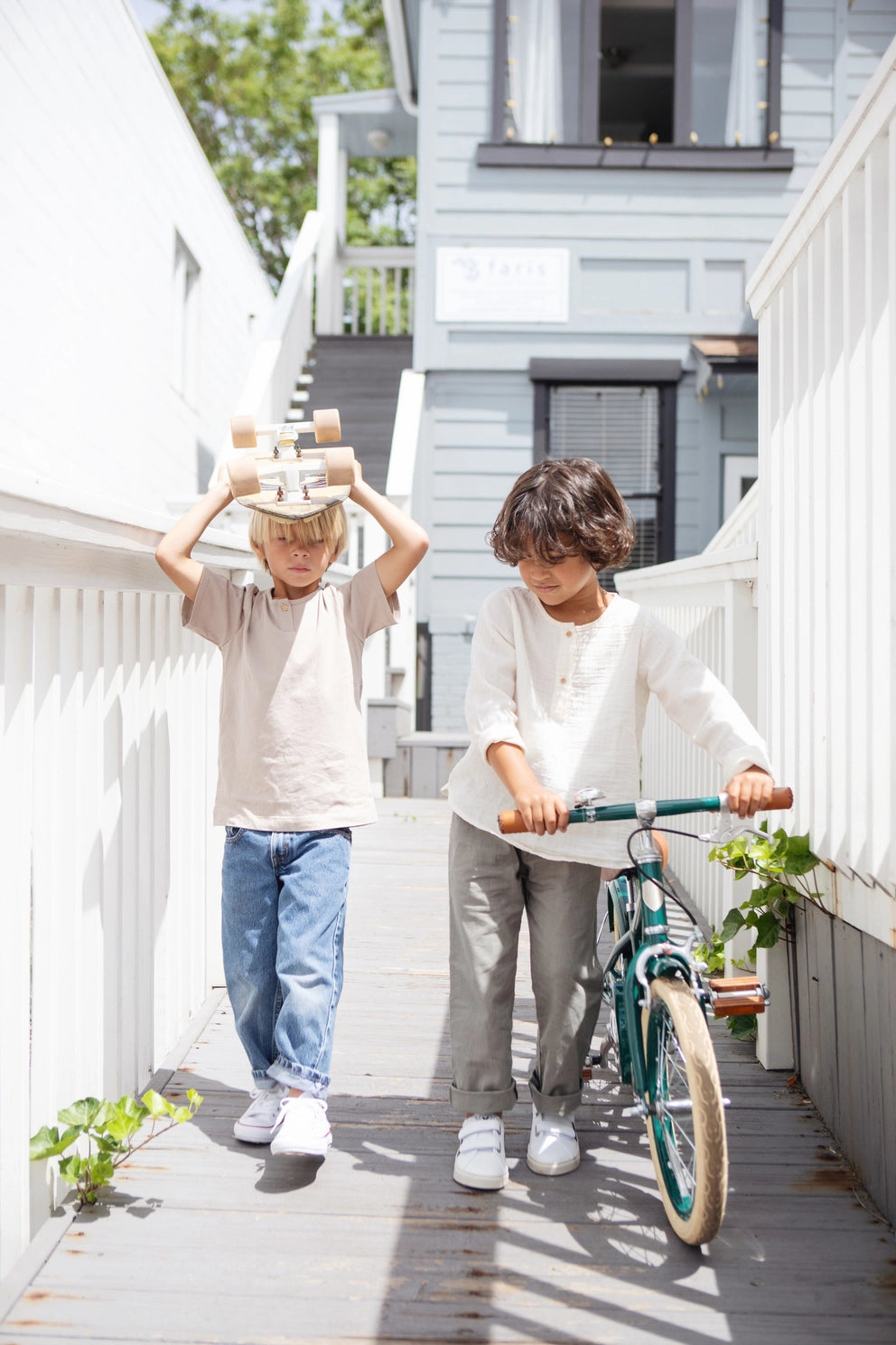 Two children on a wooden deck with one holding a toy and the other with a bicycle.