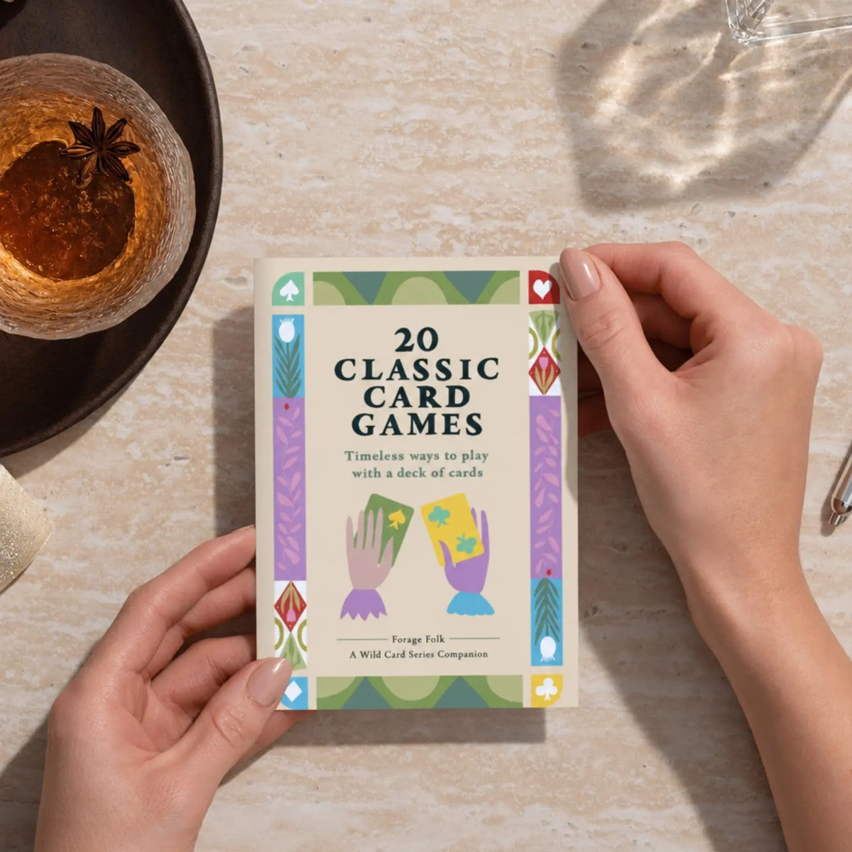 A person holds a boxed card game called "20 Classic Card Games" over a light stone tabletop