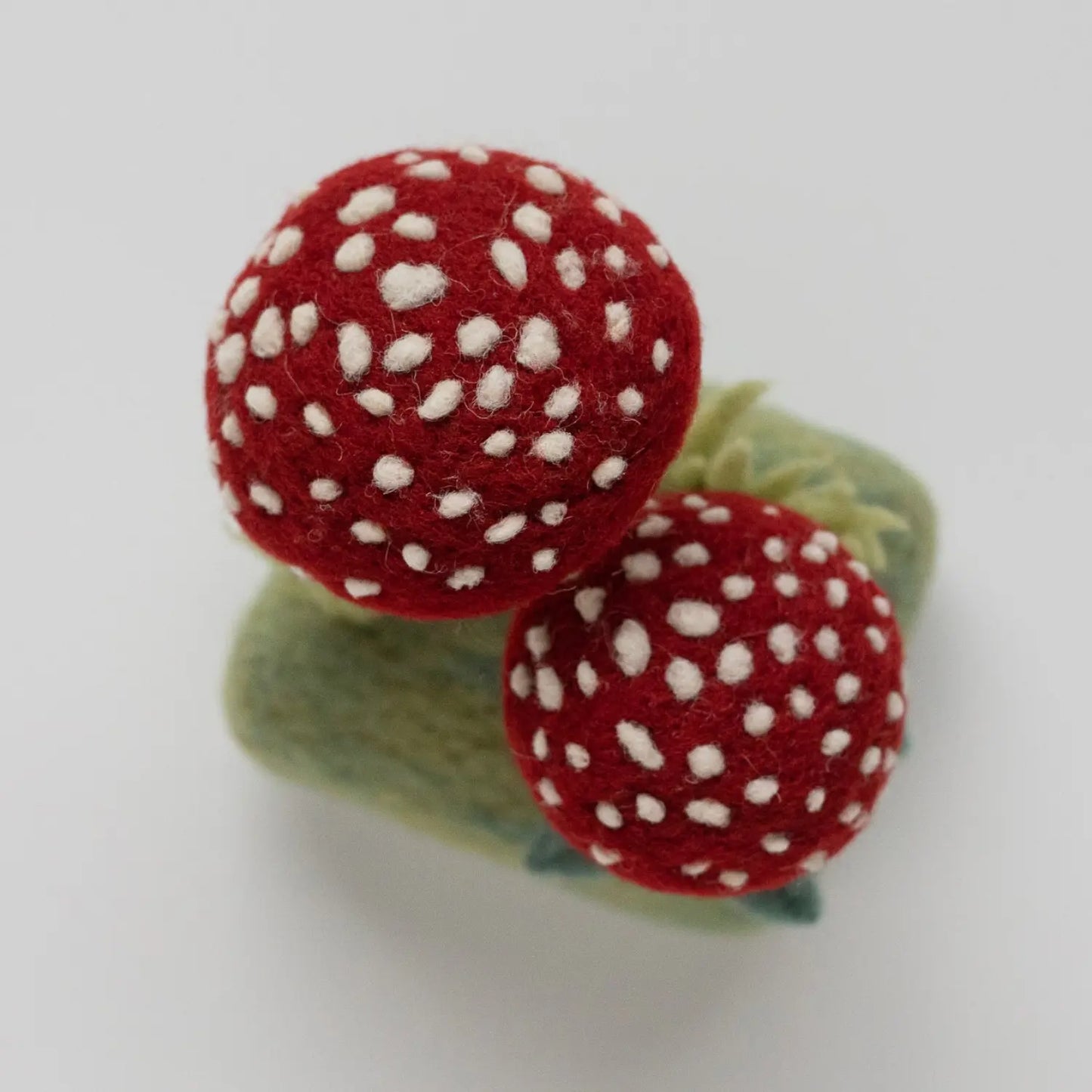 Top view of two red and white needle felted toadstools on a wool base