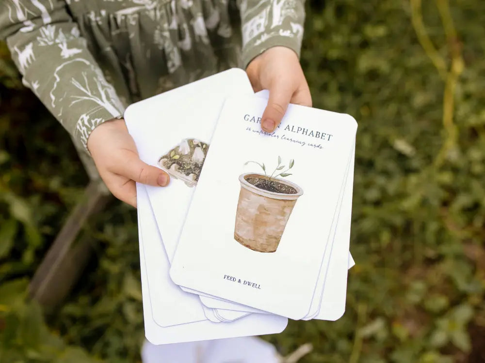Child holding multiple garden alphabet cards for early literacy learning