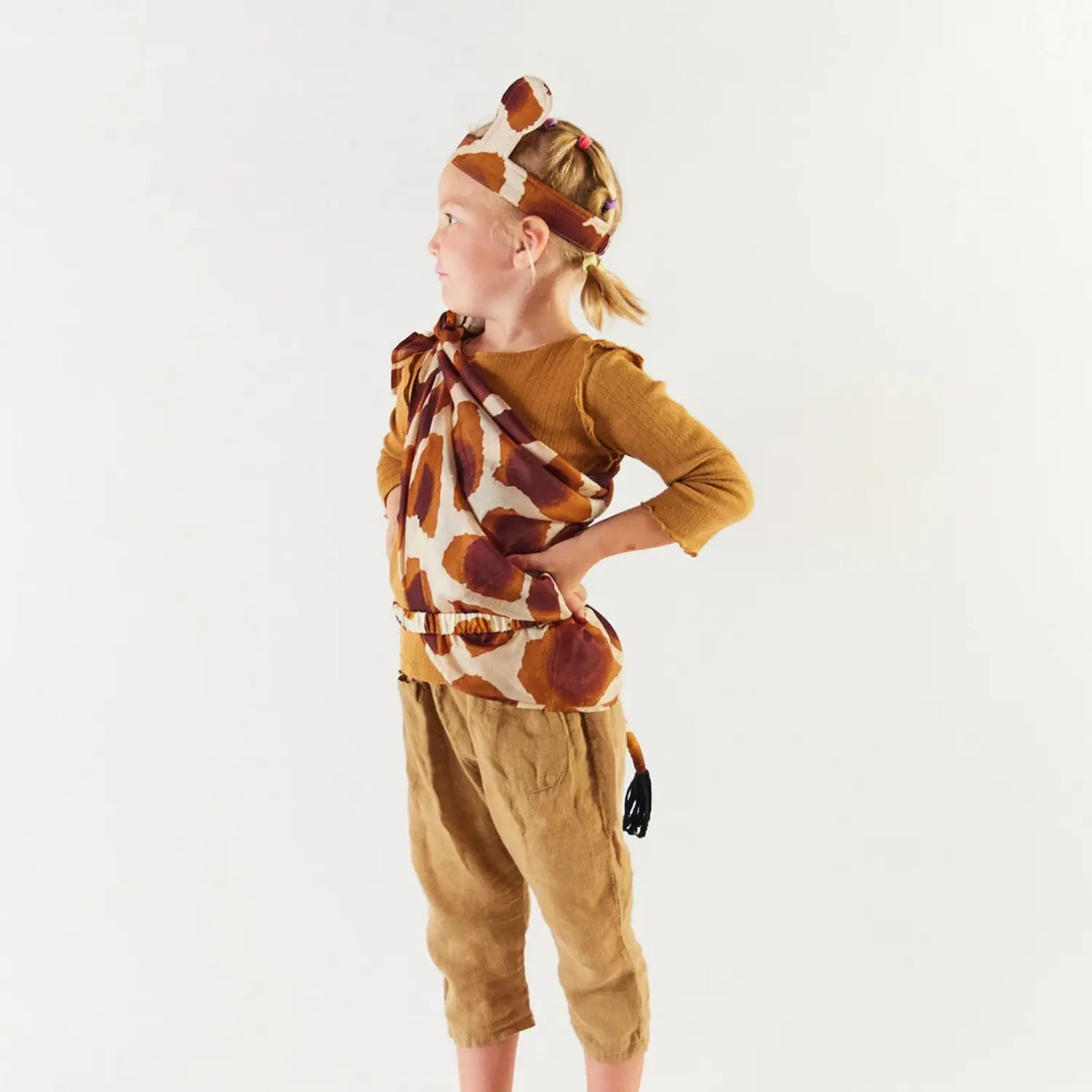 Child in a giraffe dress-up costume with silk giraffe ears, a giraffe print playsilk and a tail
