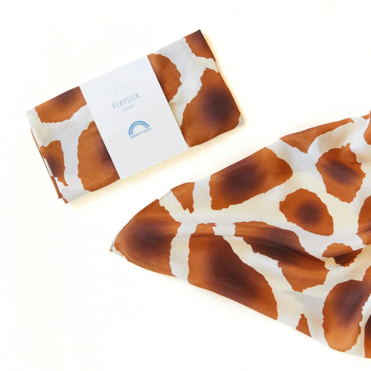 Giraffe Playsilk folded in its Sarah's Silks package beside the unfolded silk showing the spotted print
