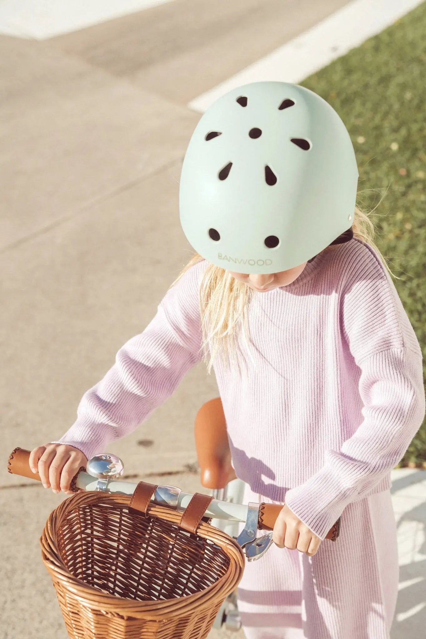 Child wearing a light green helmet with black dots, standing next to a bicycle with a basket.