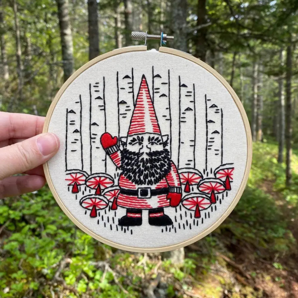 Finished gnome embroidery hoop held outdoors in a forest setting