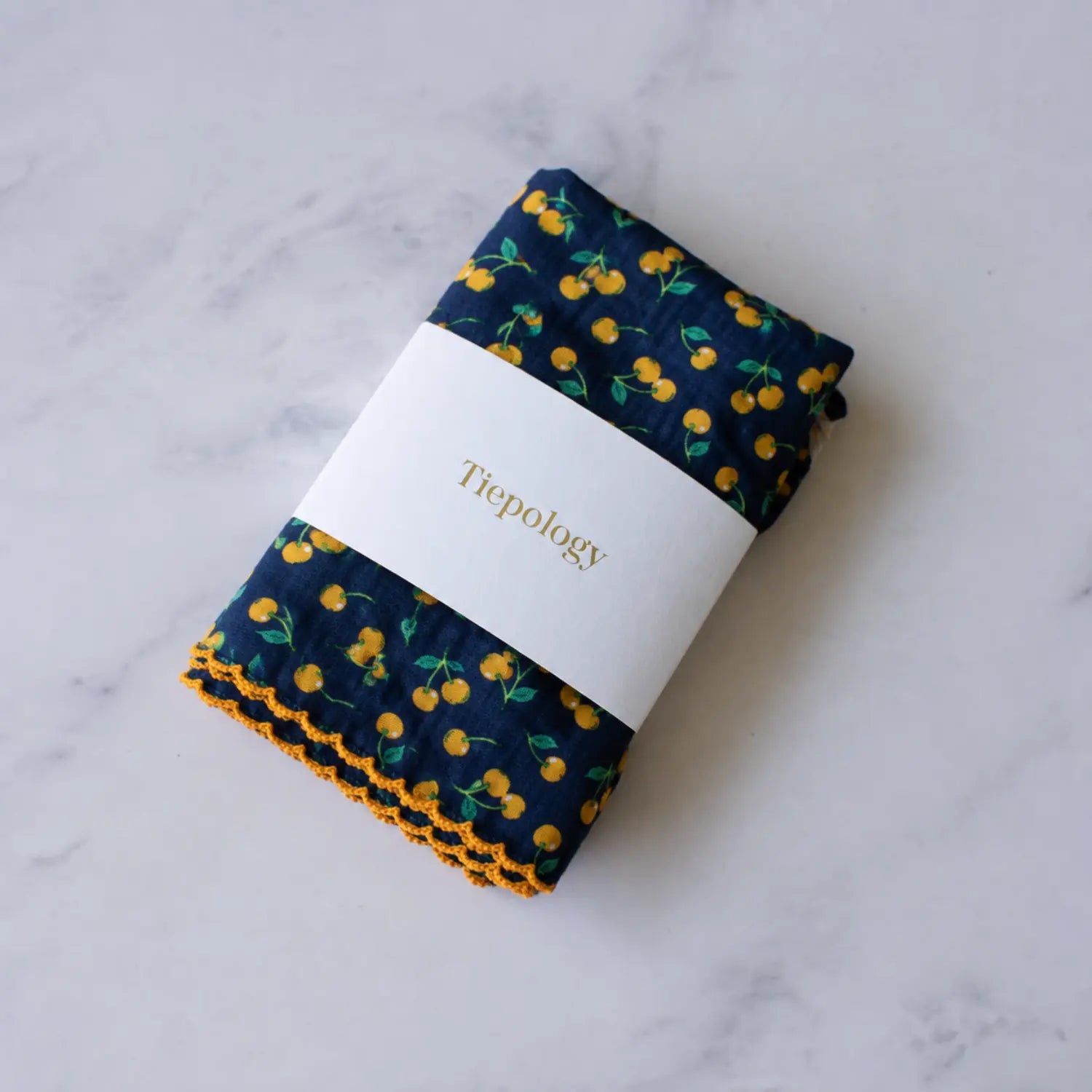 Folded Golden Cherry reusable lunch napkin by Tiepology in a navy blue cherry print with orange edging