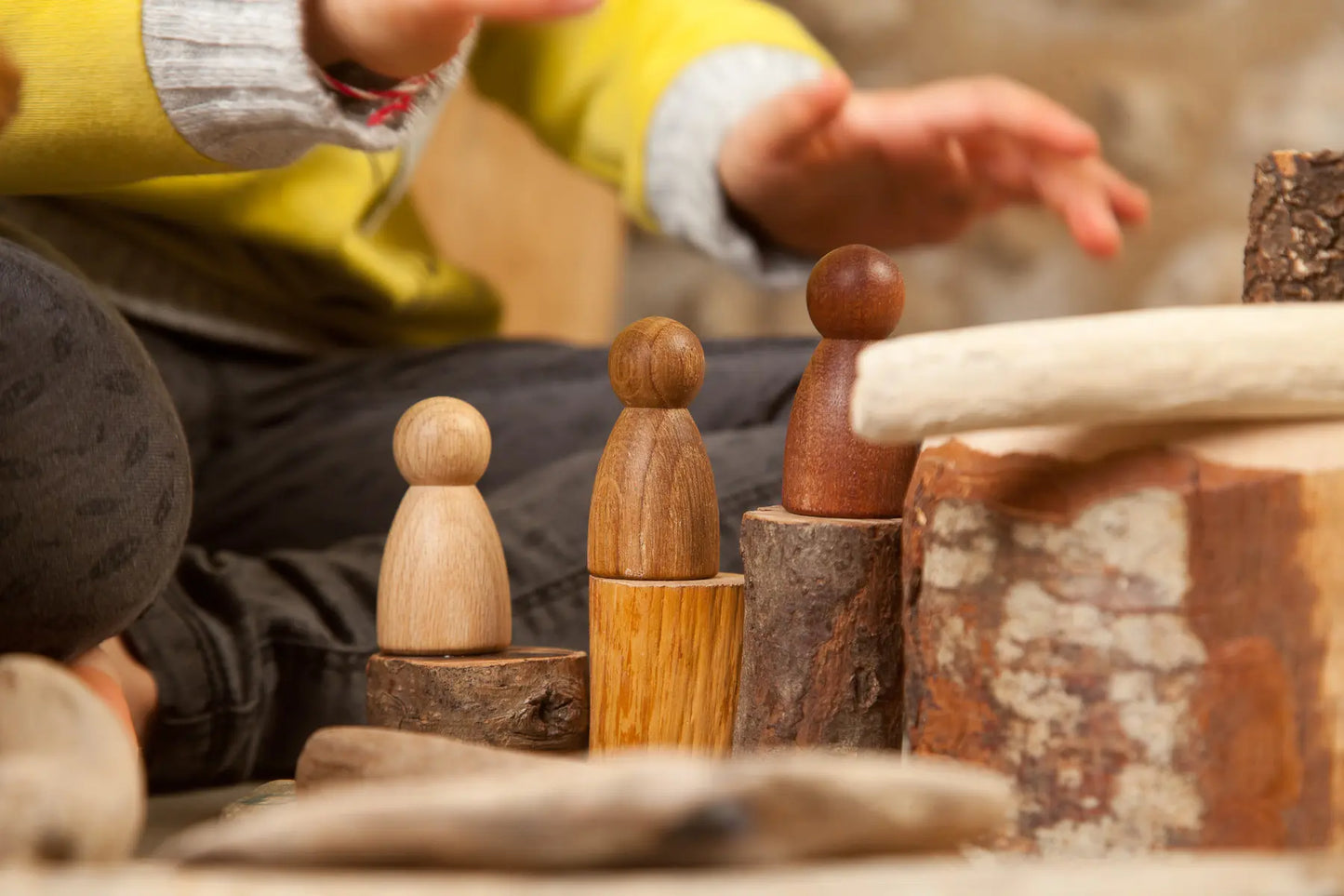 Child playing with Grapat 3 Nins 3 Woods wooden peg dolls in a natural small-world scene.