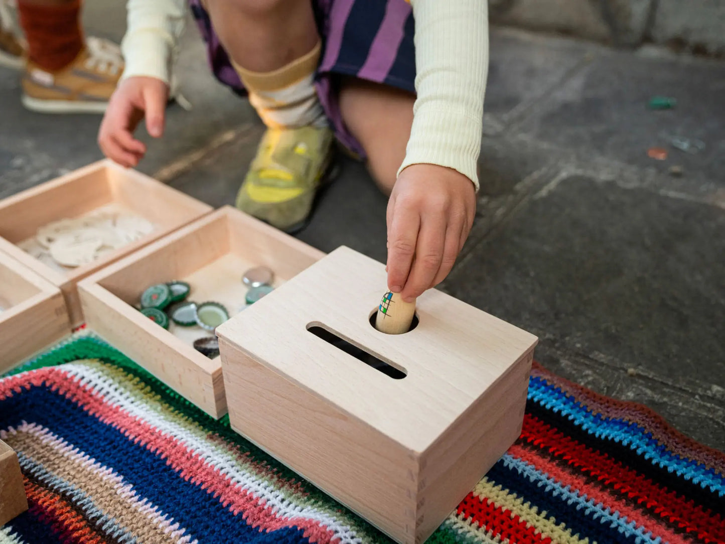 Child playing with a wooden treasure box on a colorful rug