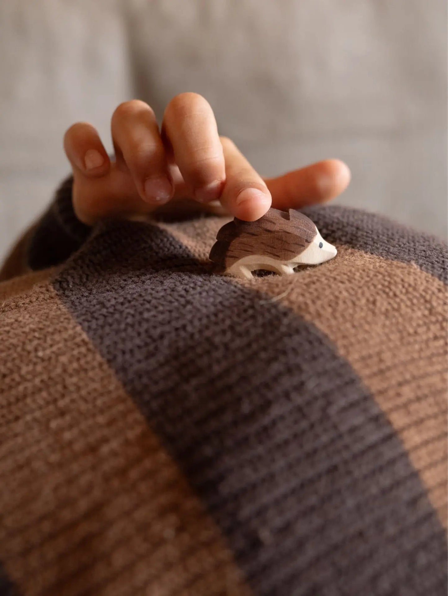 Child's hand holding a small Ostheimer wooden hedgehog figure on a striped fabric surface