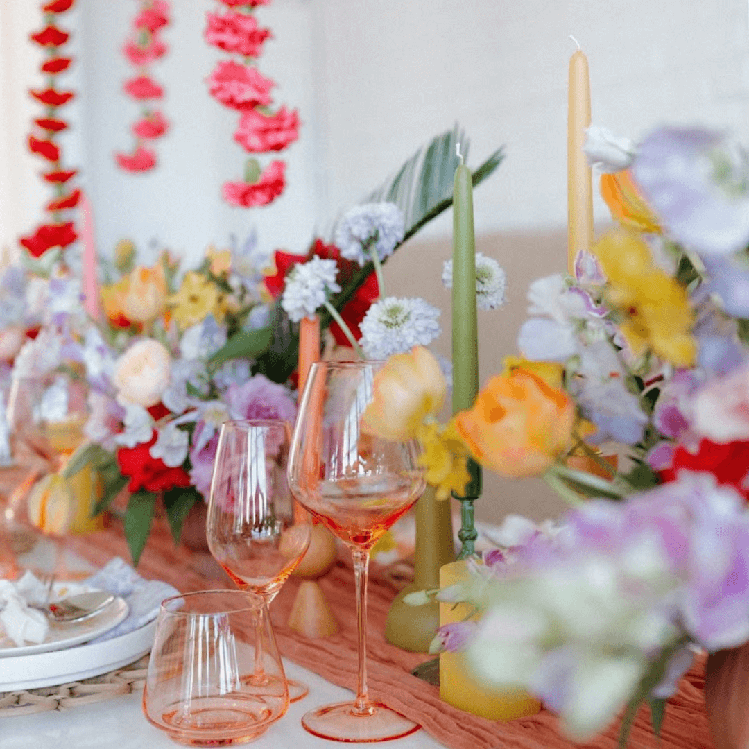 Decorative table setting with flowers, candles, and glasses on a white surface.