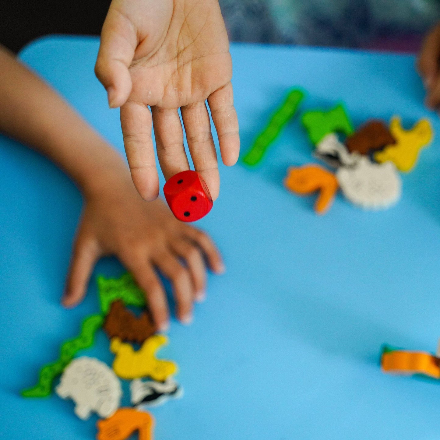 Child's hand holding a red toy figure on a blue surface with other toys.