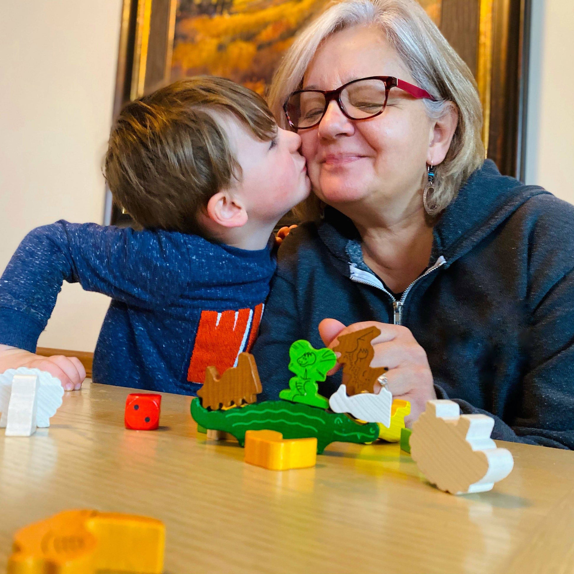 Child kissing an adult on the cheek while playing with toys at a table.