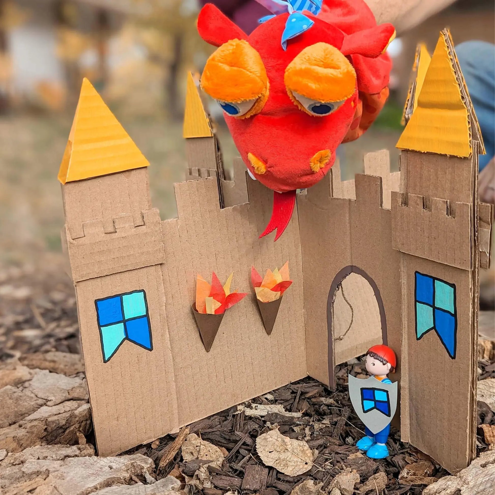 Cardboard castle with dragon puppet and knight toy figures outdoors