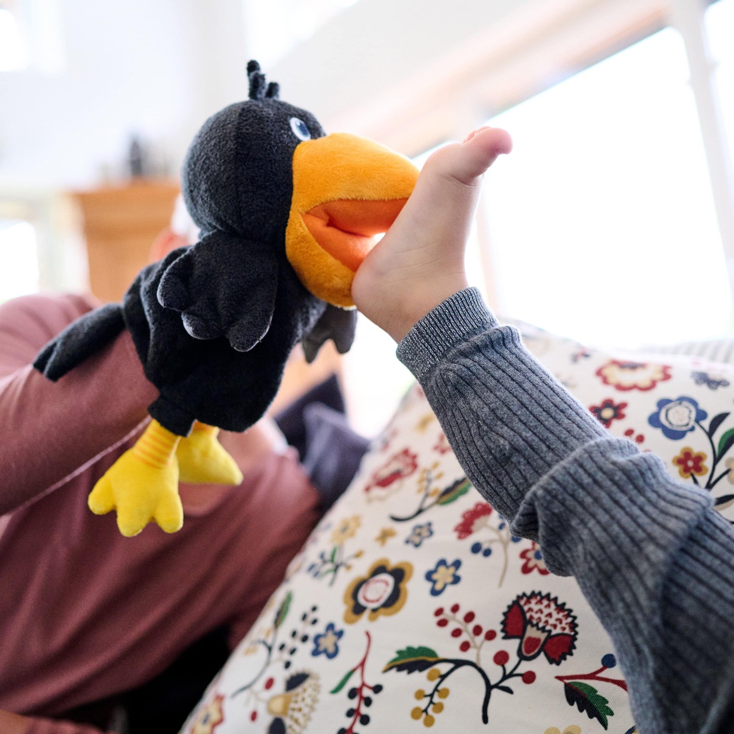 Person holding a plush toy resembling a bird with an orange beak on a floral-patterned couch.