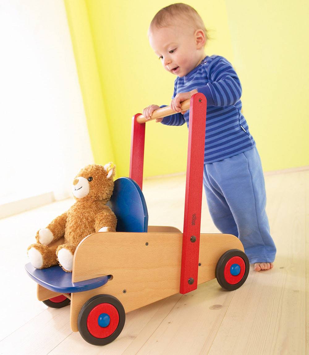 Child playing with a wooden toy cart with a plush animal inside on a light wood floor.