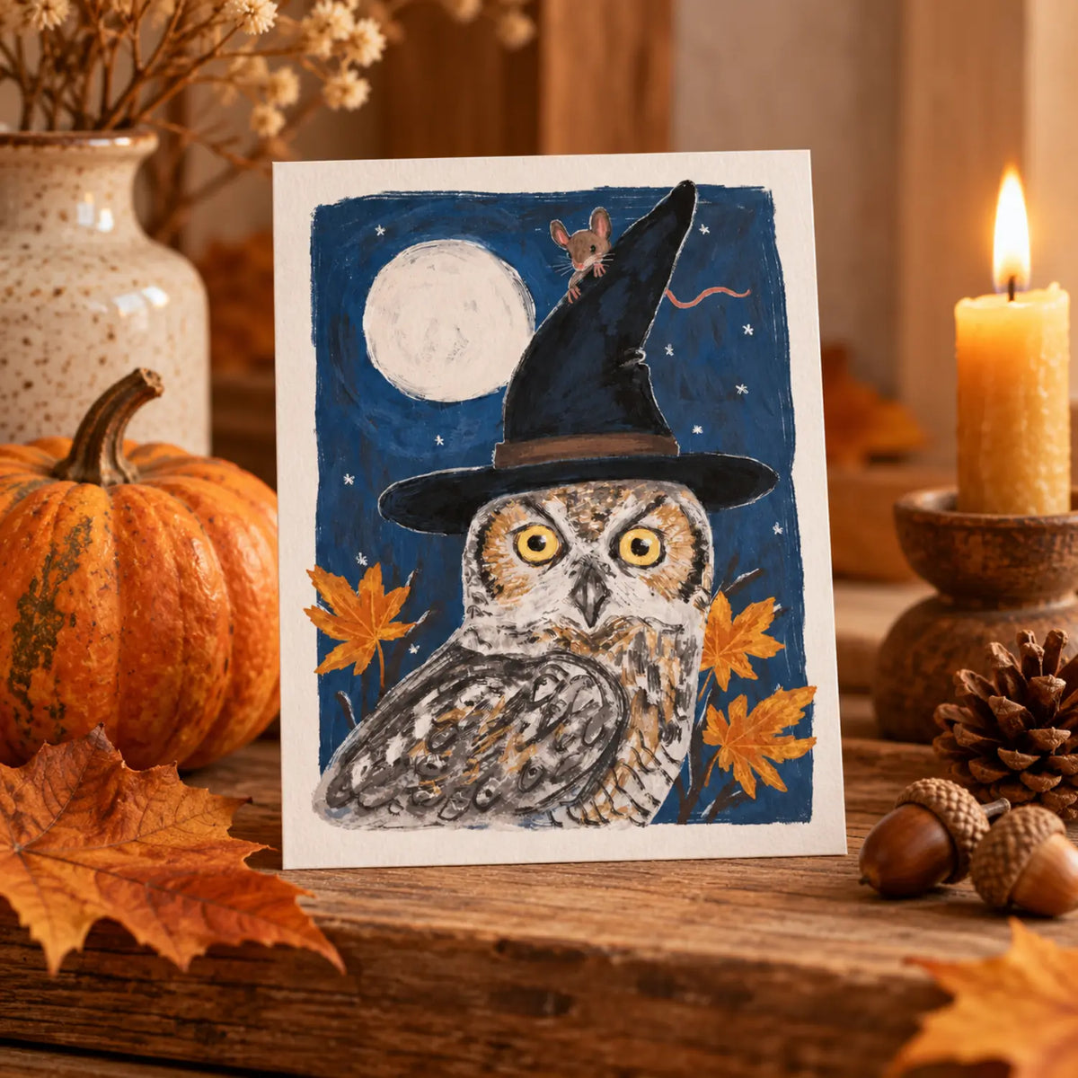 Halloween owl and mouse postcard with witch hat and full moon displayed on an autumn nature table with pumpkin, leaves, acorns and candle.