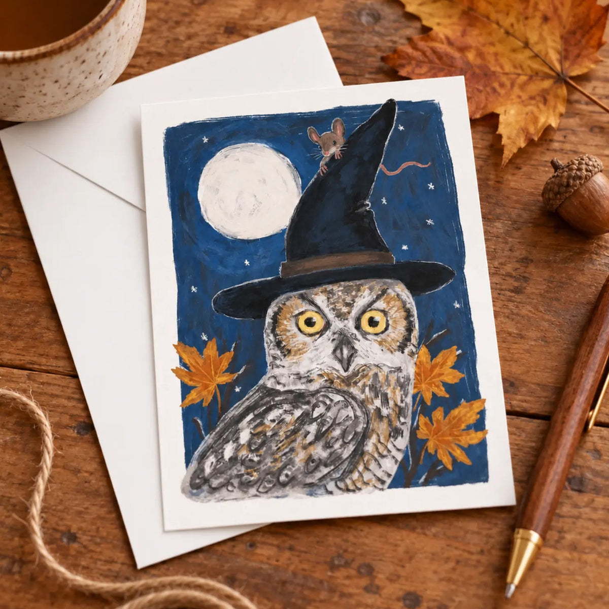 Halloween owl and mouse postcard with witch hat, full moon and autumn leaves styled on a cozy writing desk with a white envelope.