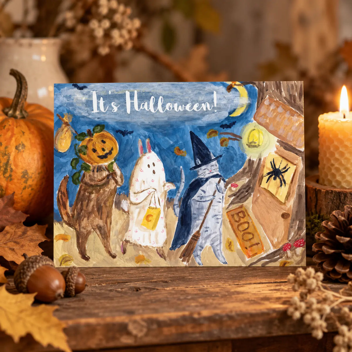 Halloween Parade woodland postcard with costumed animals displayed on an autumn nature table with pumpkin, beeswax candle, acorns and pinecone.