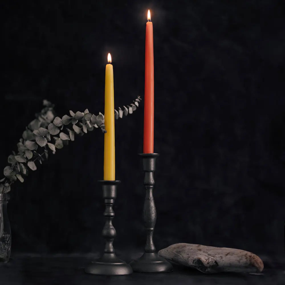 Two candles, one yellow and one red, in black candlesticks on a dark background.