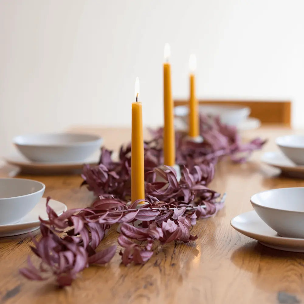 Decorative table setting with purple leaves and yellow candles on a wooden table.