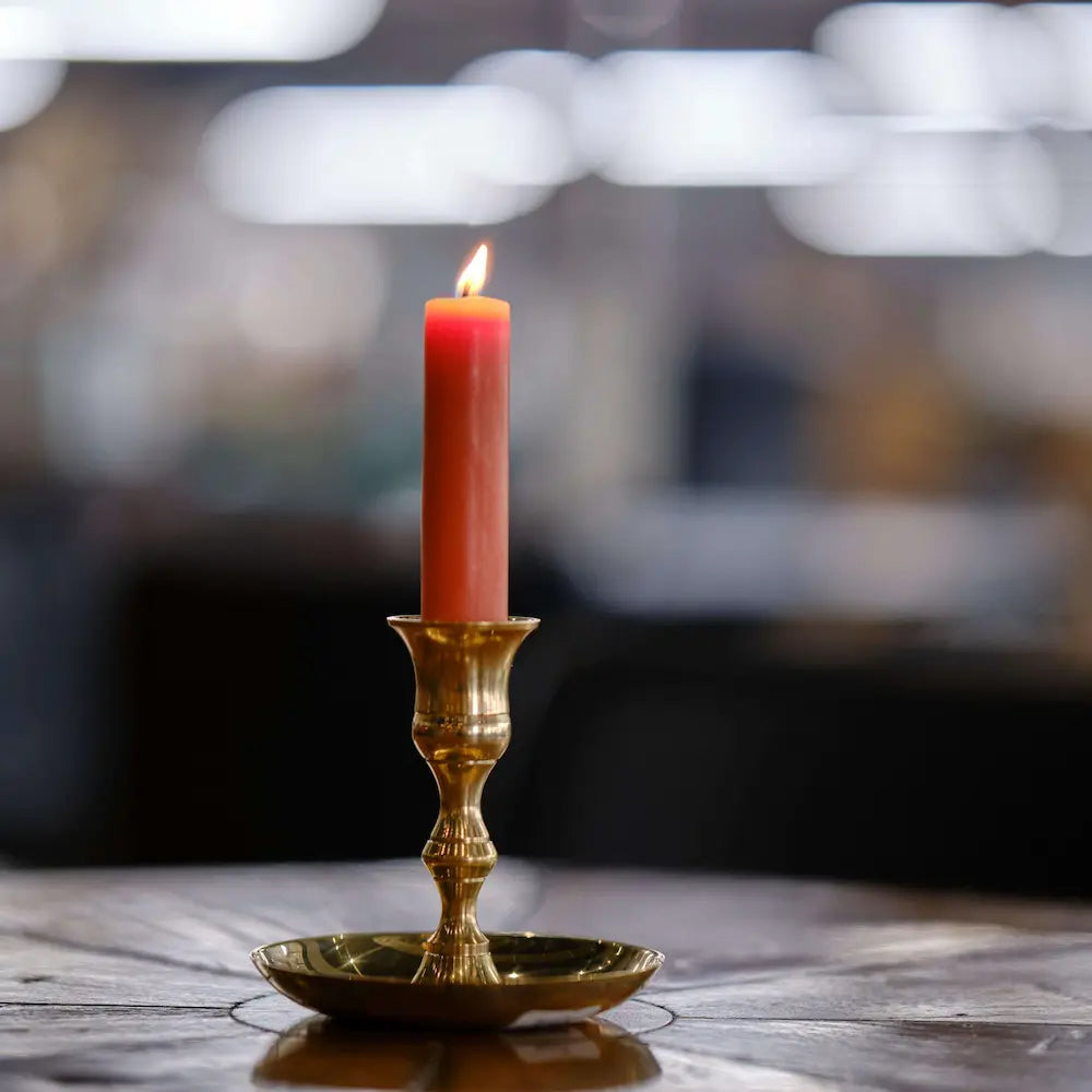 Red candle in a brass candlestick holder on a wooden surface with a blurred background