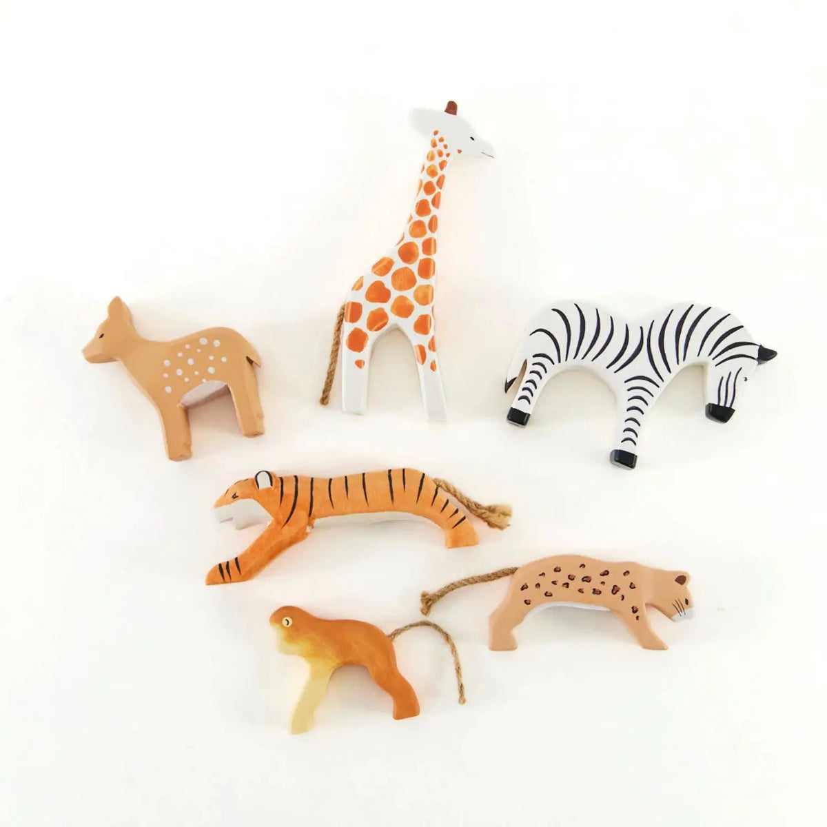 Flat lay of hand-painted wooden animals by Sarah’s Silks: giraffe, fawn, zebra, tiger, cheetah, and monkey