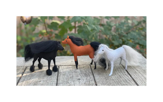 three finished felt horses made from the hand sewing felt horse kit standing outside