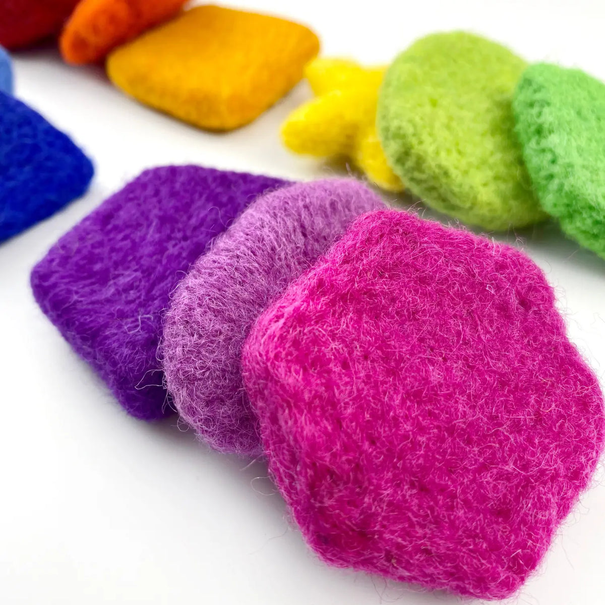 Close-up of handmade wool felt sorting shapes in pink, purple, and green, showing their soft felted texture.