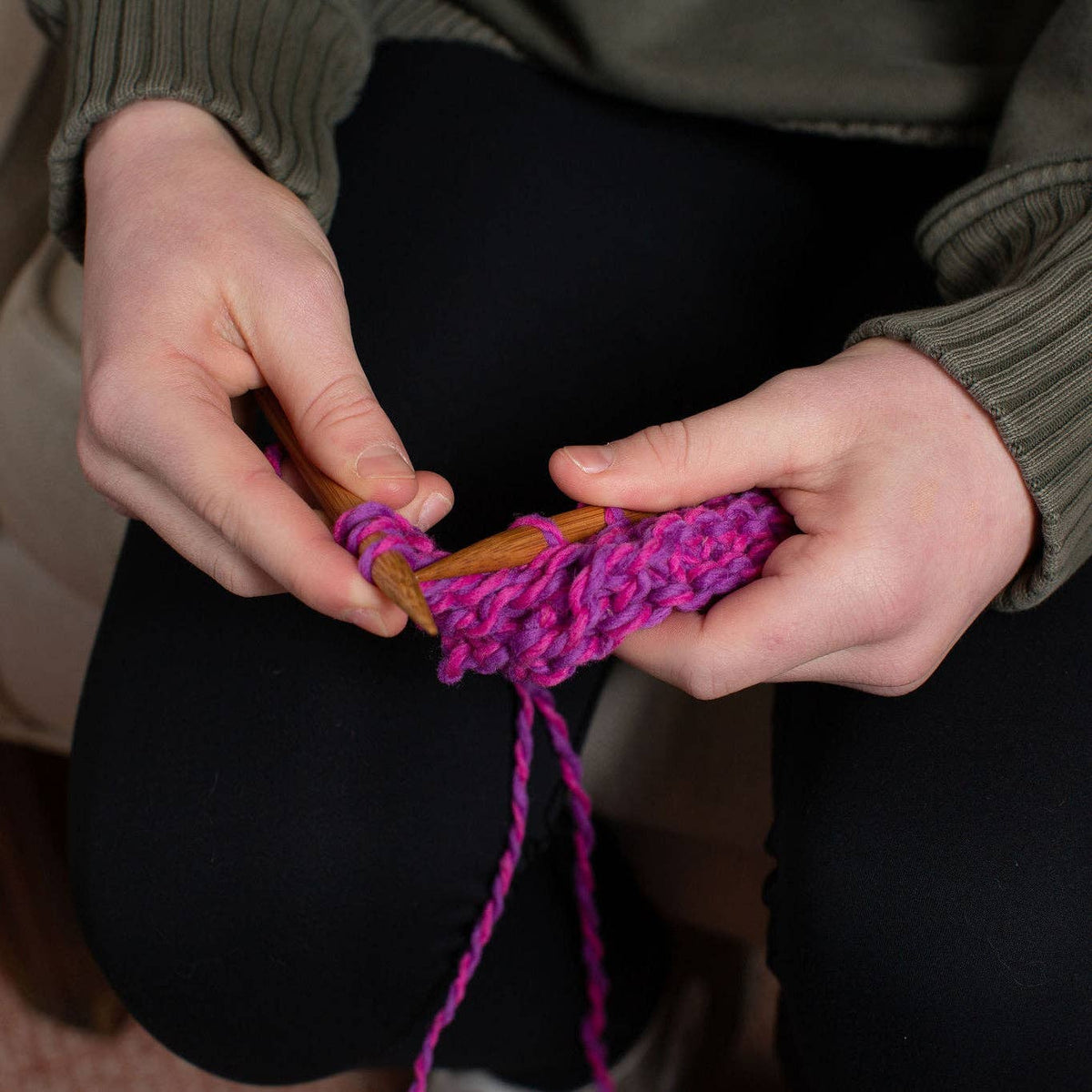 Close-up of hands knitting garter stitch rows on wooden needles with wool yarn