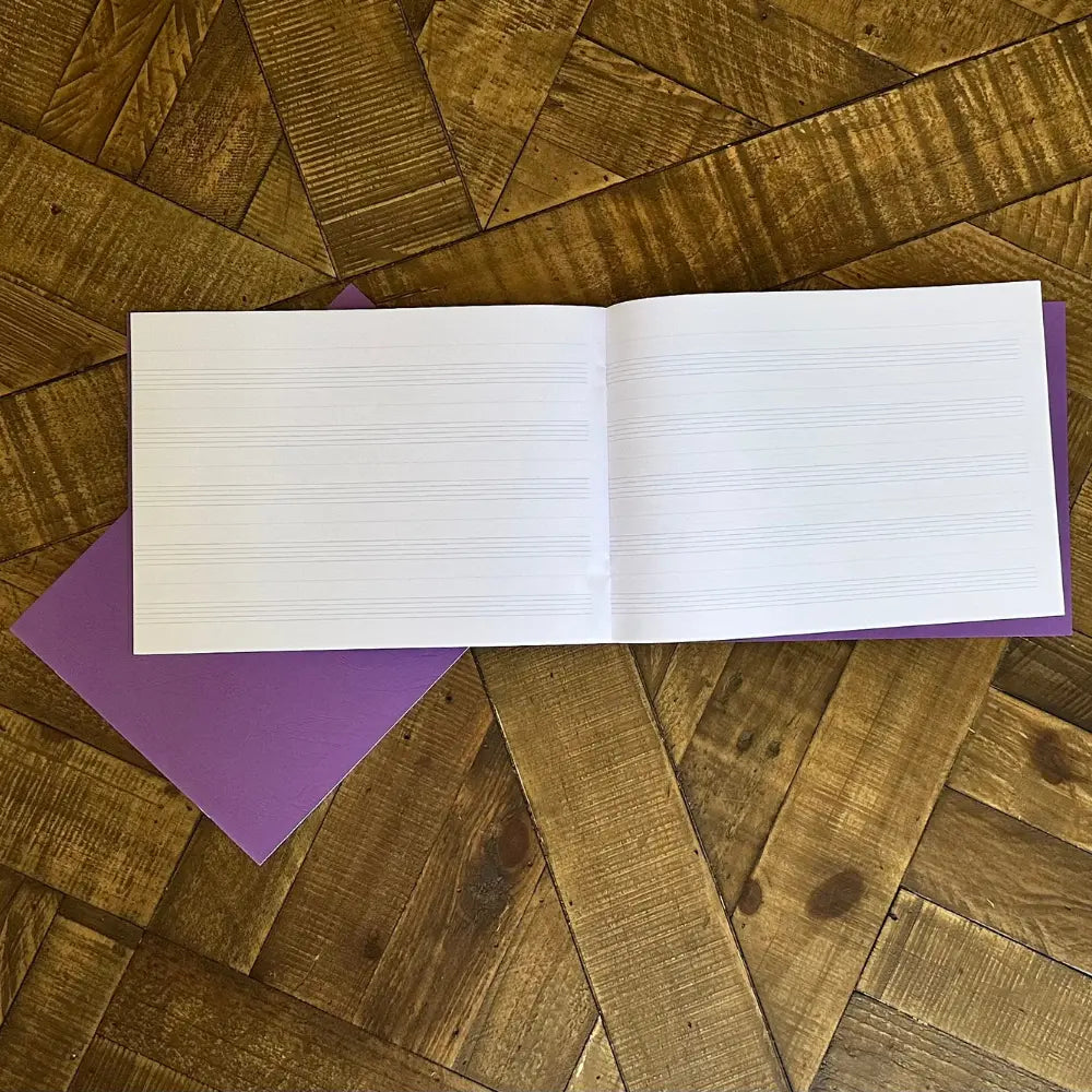 Open music notation notebook with lined pages on a wooden surface