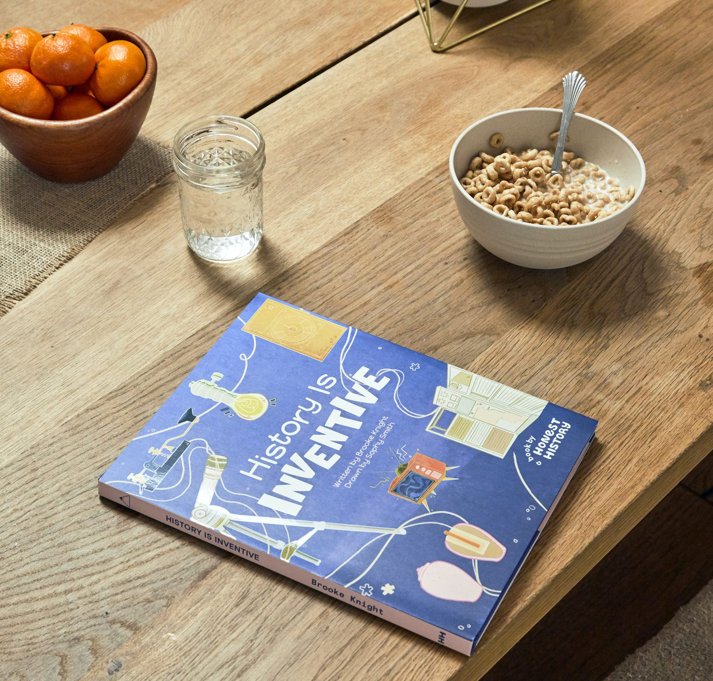History Is Inventive children’s book displayed on a wooden table next to a bowl of cereal in a home setting